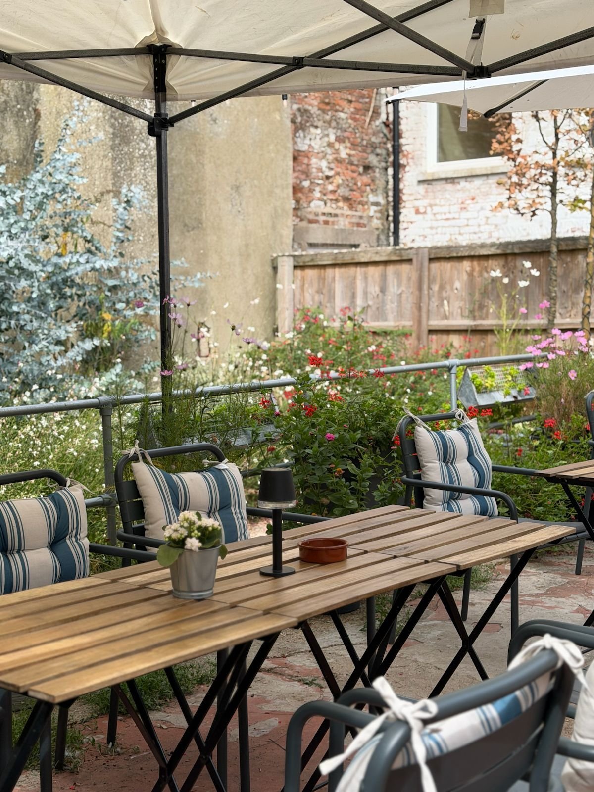 Wadhams courtyard with wooden tables, striped chairs and potted flowers under the canopy