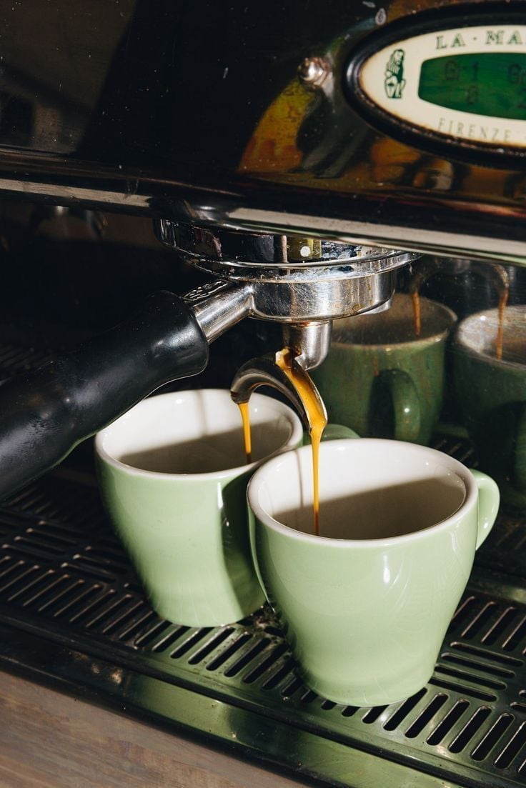 Espresso pouring from the machine into two green ceramic cups